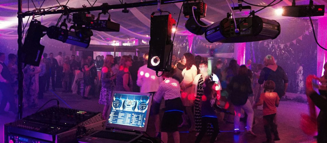 A moody scene capturing the Nightsound Disco DJ console, with lighting and effects illuminating the crowd
